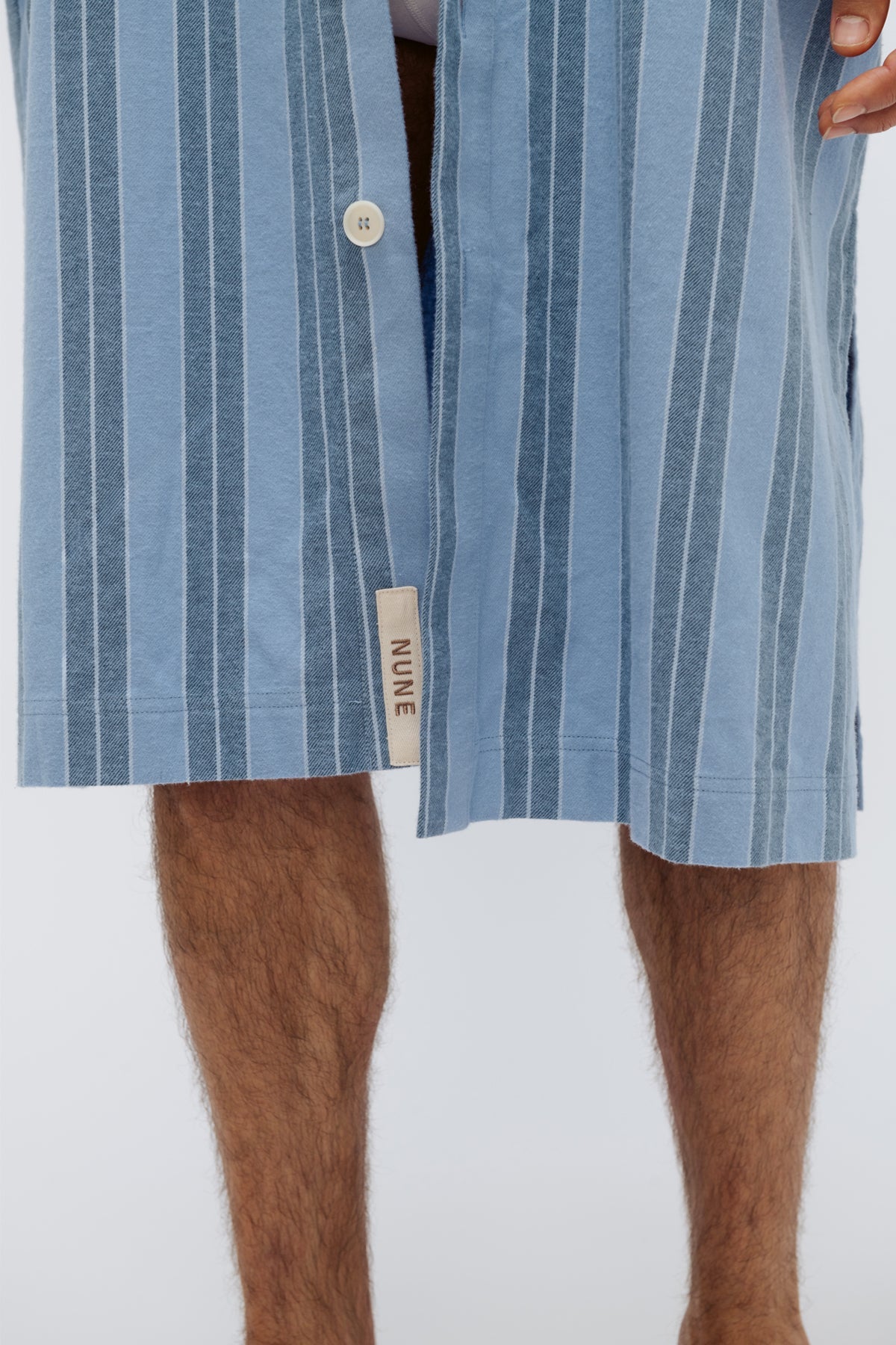 Close up of NUNE label on the front of Blue Daybreak Stripe Long House Shirt in Brushed Cotton Flannel with male model's legs