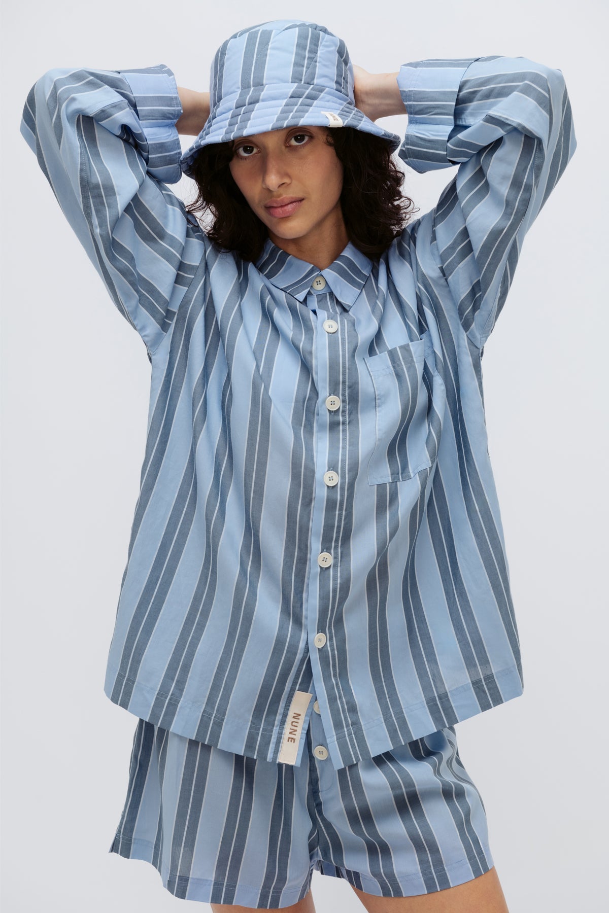 Long Sleeve Sleep Shirt Macel, Boxer Short and Doona Hat all in Daybreak Stripe worn by female model holding her hands behind her head, cropped front view.
