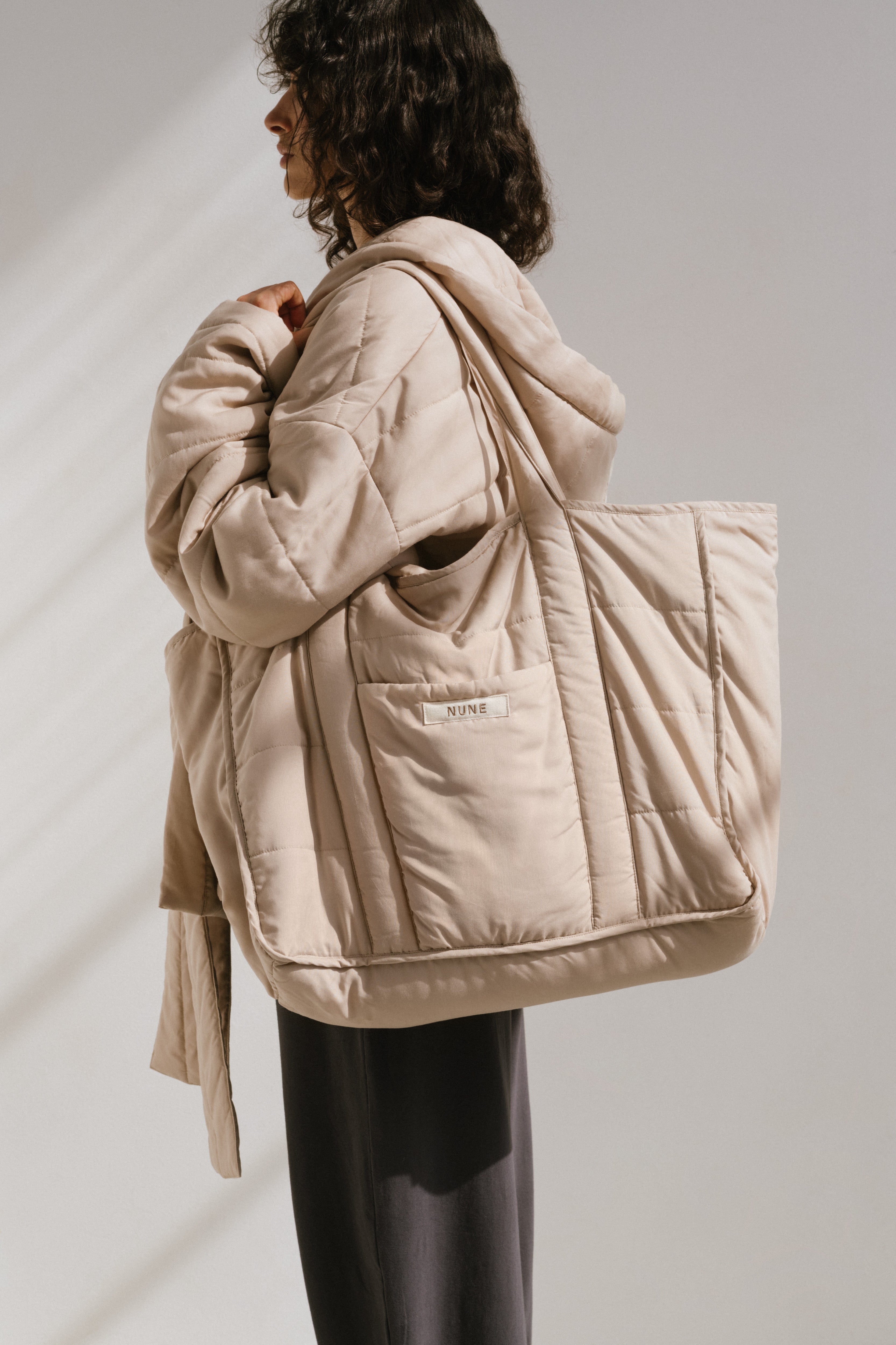 Doona Tote in Oat and Doona Short Robe in Oat with Long Sleep Pants in Charcoal worn by female model side view showing front pocket and NUNE label