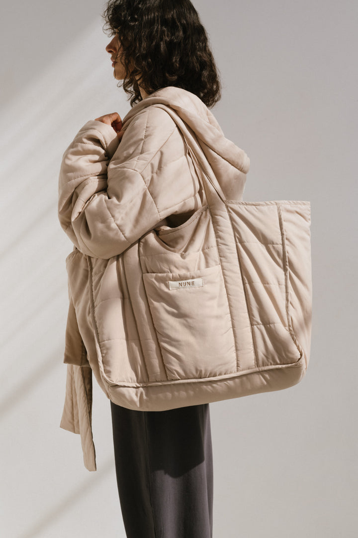 Doona Tote in Oat and Doona Short Robe in Oat with Long Sleep Pants in Charcoal worn by female model side view showing front pocket and NUNE label