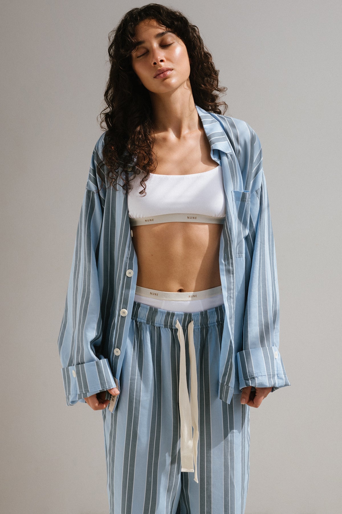 Long Sleeve Sleep Shirt and Long Sleep Pants Macel in Daybreak Stripe worn over Square Neck Bralette and High Waist Briefs in White by female model standing with her eyes closed.