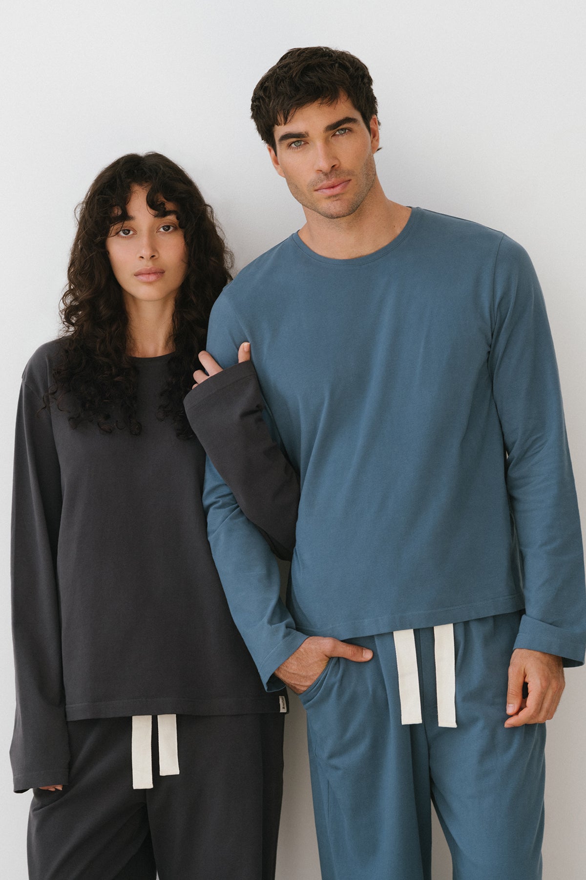 Cosy Long Sleeve Top and Cosy Pants in Noon worn by male model and Cosy Long Sleeve Top and Cosy Pants in Charcoal worn by female model standing together with arms linked