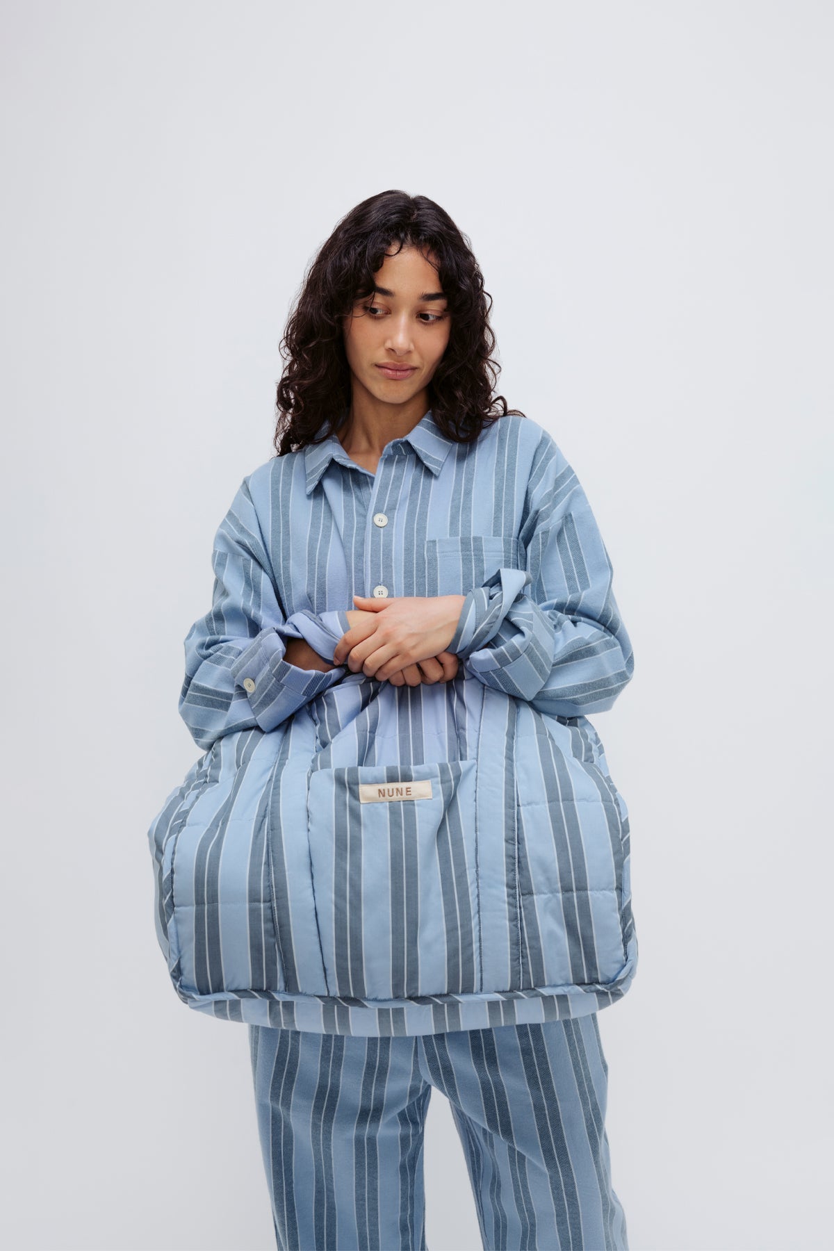 Doona Tote in Daybreak Stripe held by female model in front of her body, wearing Long Sleeve Sleep Shirt and Long Sleep Pants Flannel in Daybreak Stripe