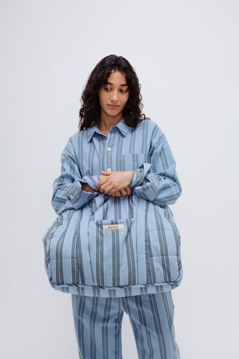 Doona Tote in Daybreak Stripe held by female model in front of her body, wearing Long Sleeve Sleep Shirt and Long Sleep Pants Flannel in Daybreak Stripe