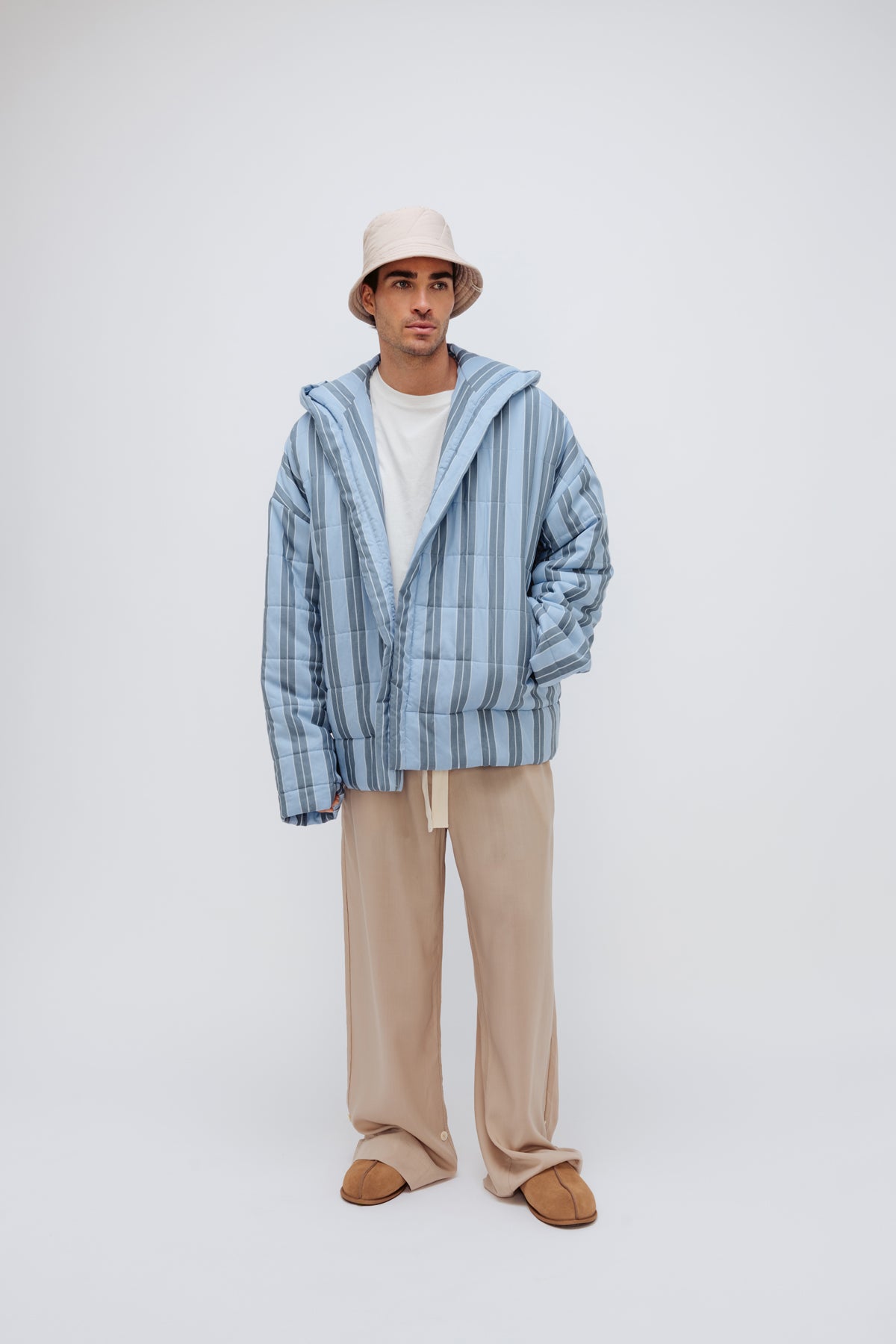 Short Doona Robe in Daybreak Stripe worn with Oat Long Sleep Pant Macel and Oat Doona Hat by male model, front view showing long length of pants and front pockets of robe.