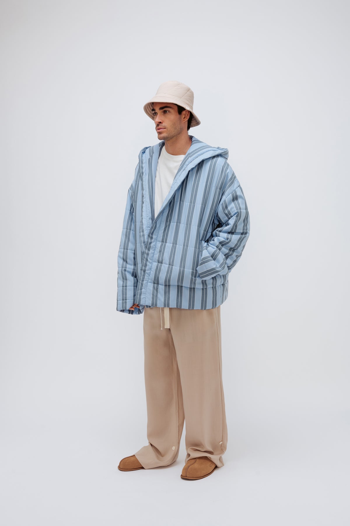 Short Doona Robe in Daybreak Stripe worn with Oat Long Sleep Pant Macel and Oat Doona Hat by male model, front side view showing long length of pants and front pockets of robe.