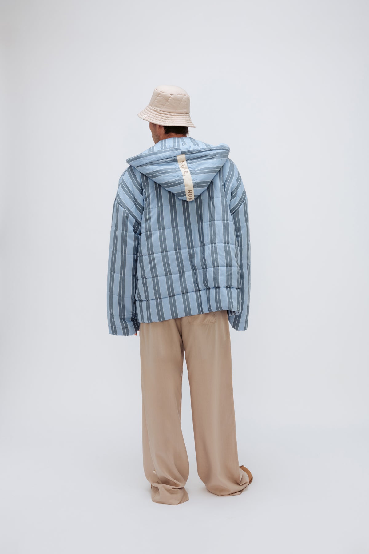 Short Doona Robe in Daybreak Stripe worn with Oat Long Sleep Pant Macel and Oat Doona Hat by male model, back view showing long length of pants.