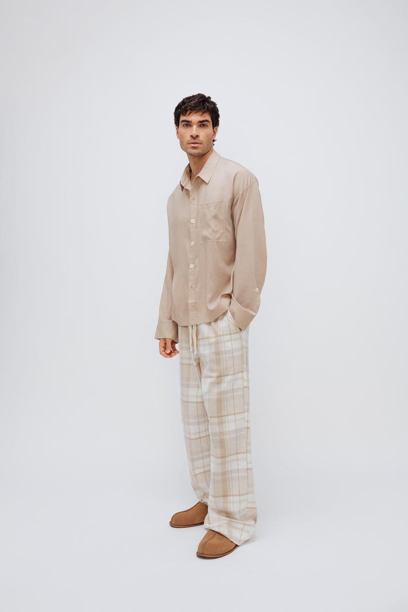 Oat long sleeve sleep shirt and flannel sleep pant in Oat Check being worn by male model, front side view showing front pocket on pants and adjustable sleeve length on shirt. 