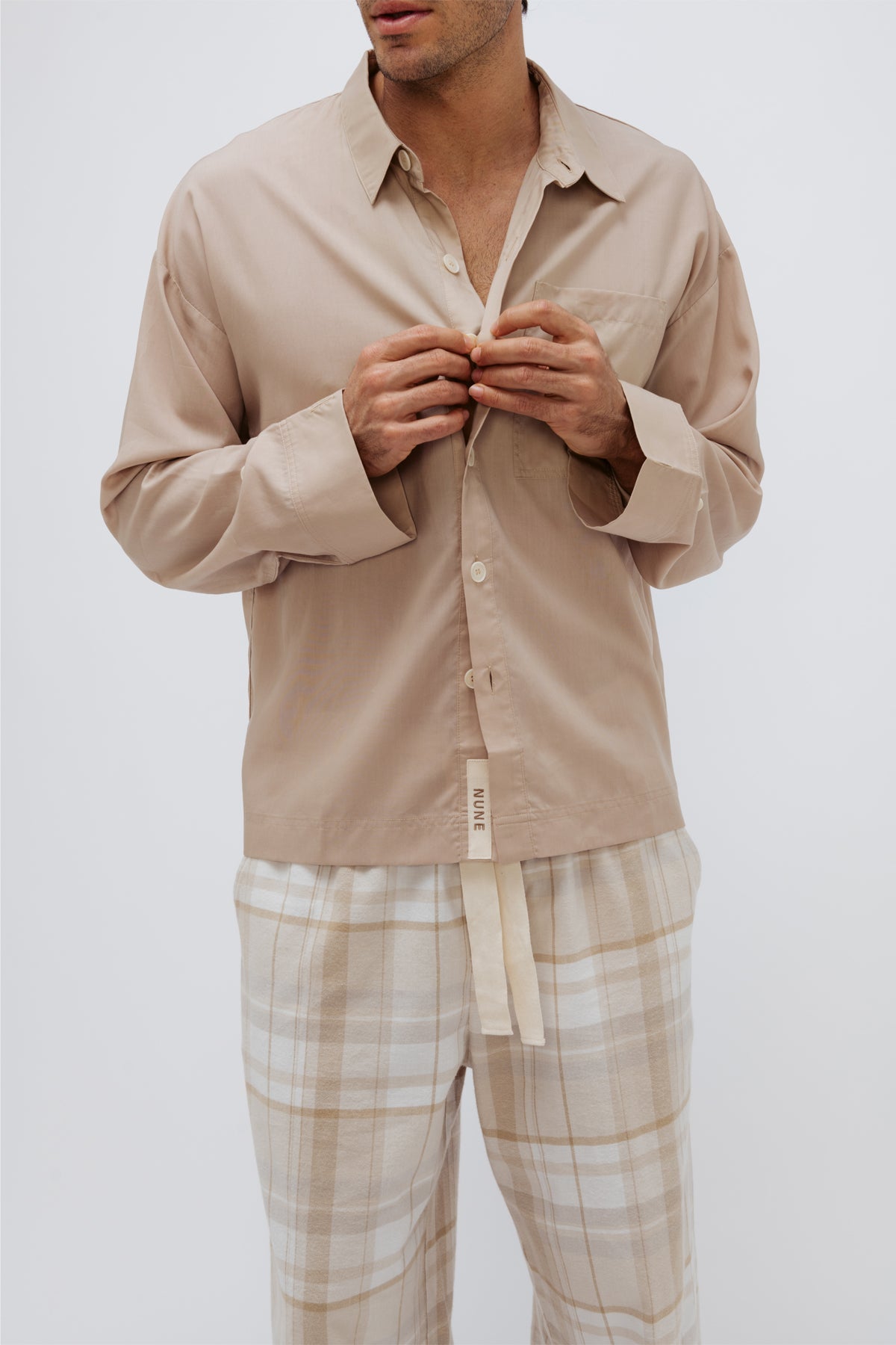 Long sleeve sleep shirt in Oat and flannel sleep pant in Oat Check being worn by male model, cropped mid-section front view showing button fastenings down front of shirt and natural cotton waist tie on pants. 