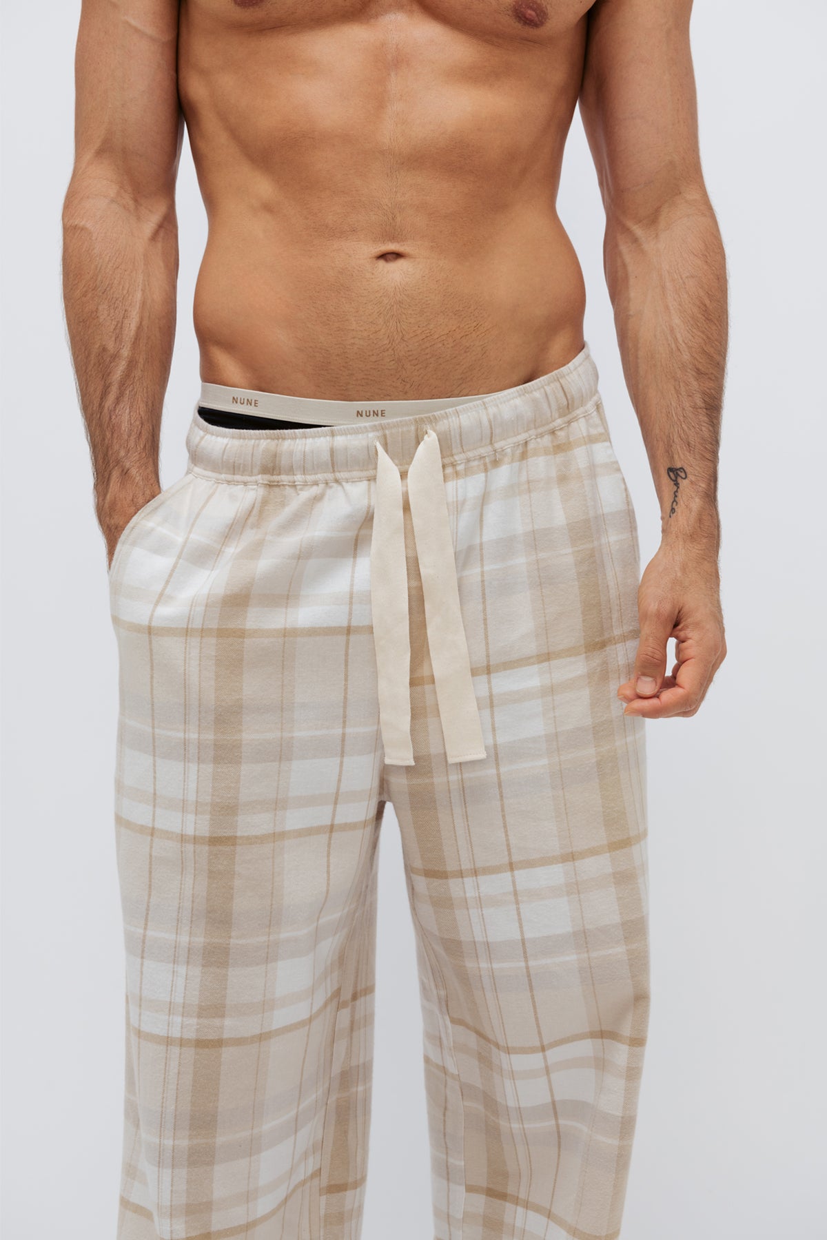 Flannel sleep pant in Oat Check being worn by male model over Men's original boxer briefs in black, cropped front side view showing NUNE soft elastic on briefs and natural cotton waist tie on pants. 