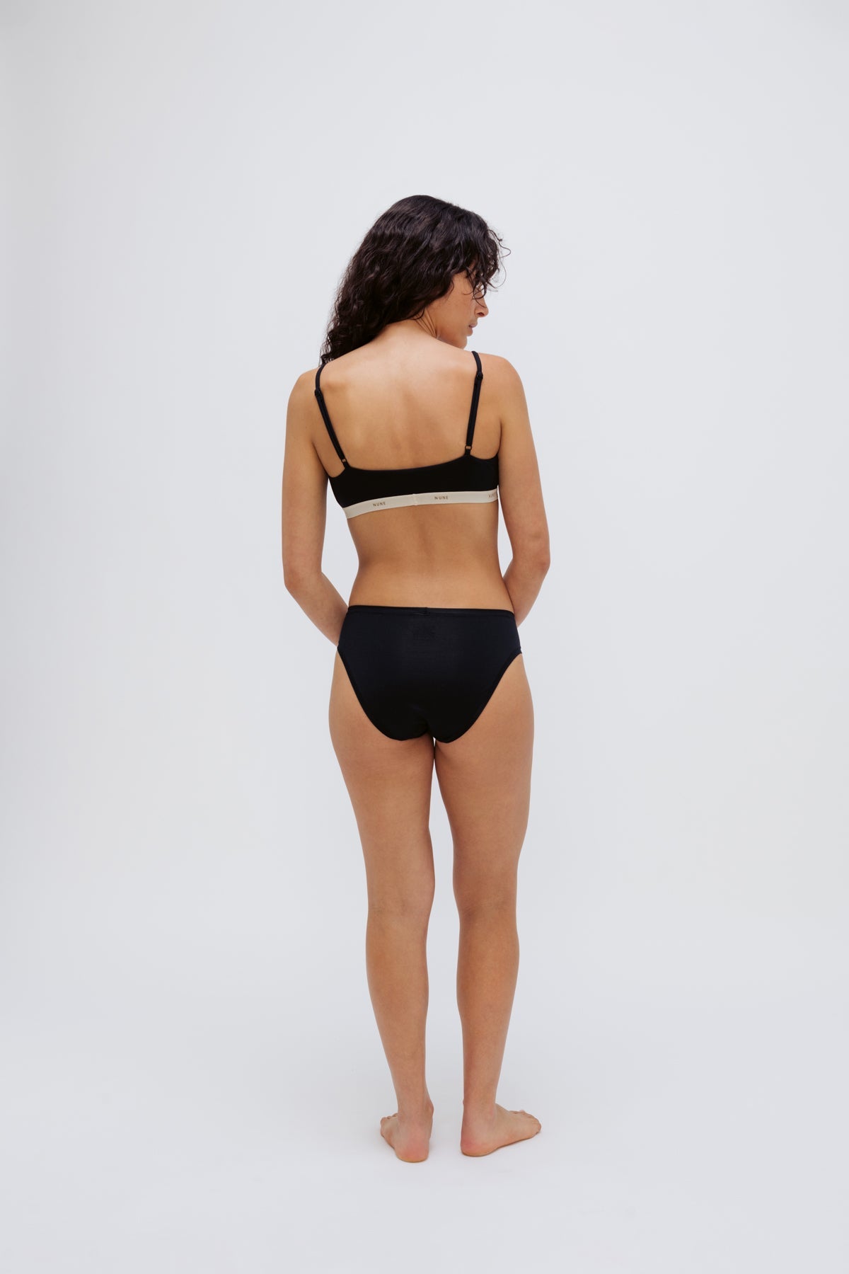 Triangle Bralette in Black and mid brief in black worn by female model, back view showing adjustable straps on bralette