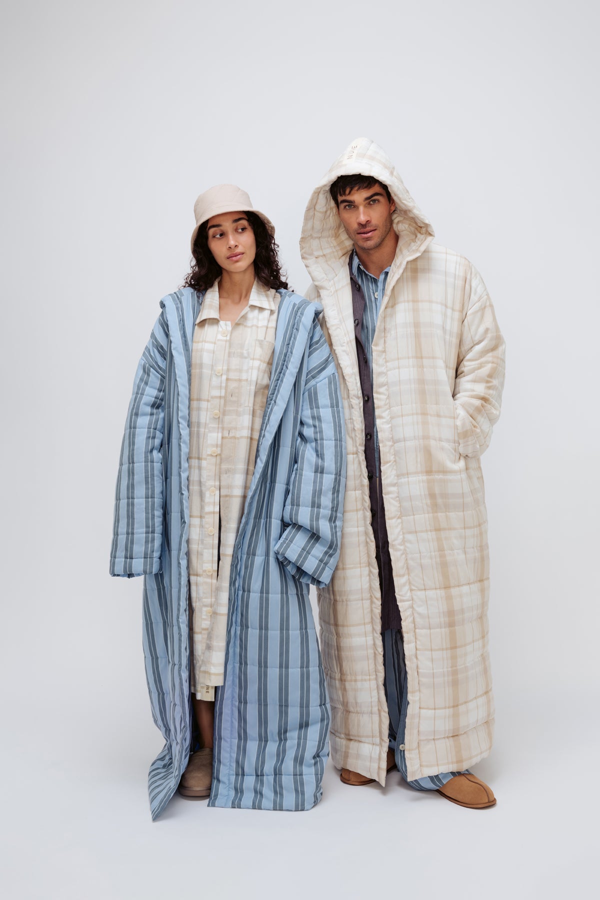 Long Doona Robe in Daybreak Stripe layered over Oat Check House Shirt worn by female model with Oat Doona Hat, and Long Doona Robe in Oat Check layered over Long Sleeve Sleep Shirt in Daybreak stripe by male model, close up front view with hood pulled over his head