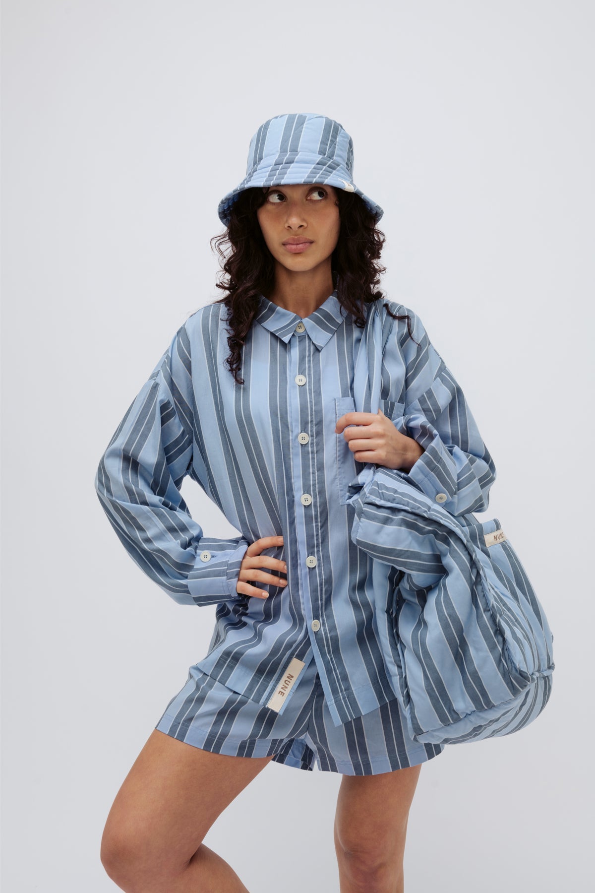 Long Sleeve Sleep Shirt Macel, Boxer Short and Doona Hat all in Daybreak Stripe worn by female model holding Doona Tote in Daybreak Stripe over shoulder.