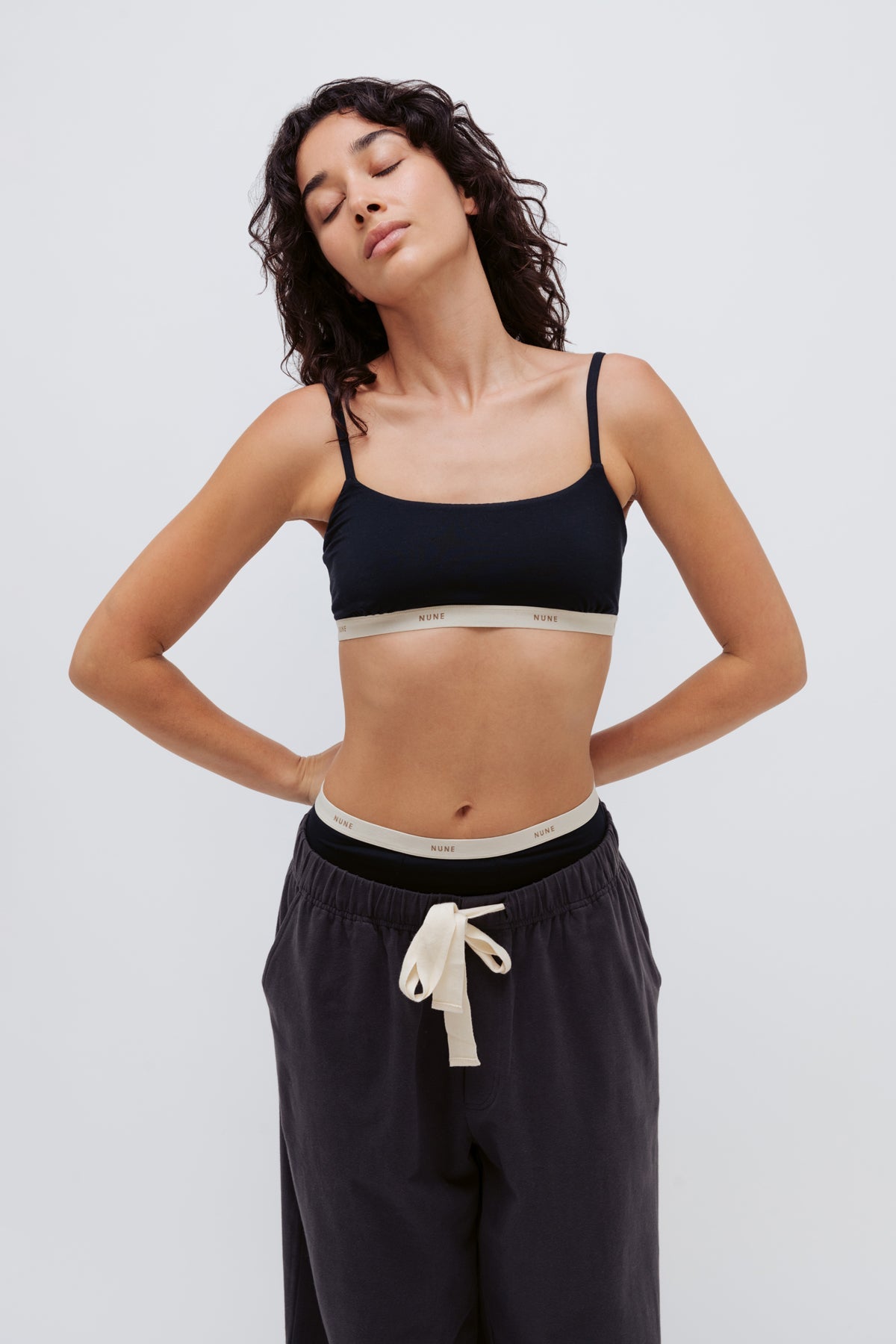 Square Neck Bralette and High Waist Brief in black worn by female model under Cosy Sleep Pant in Charcoal standing with arms behind her back and eyes closed