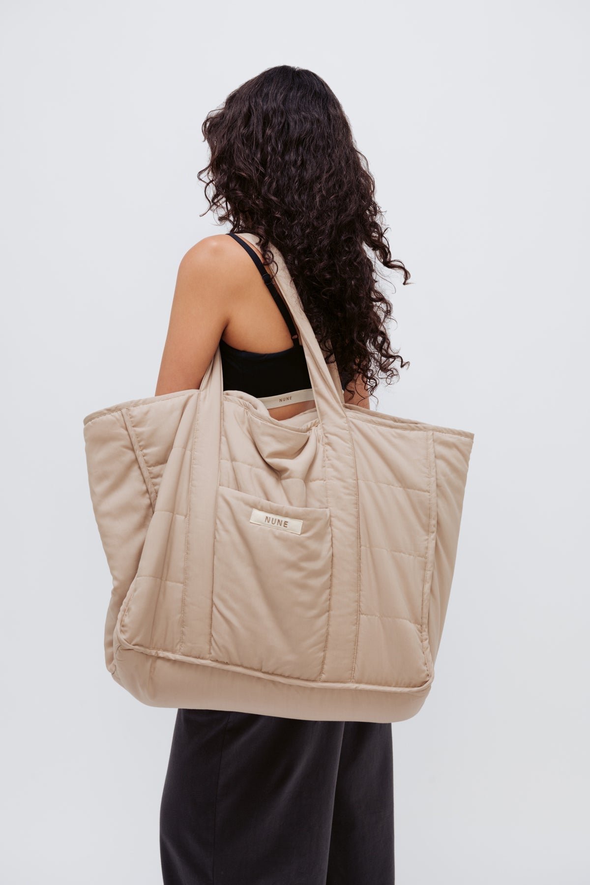 Oat Doona Tote worn over the shoulder of female model wearing Black Square Neck Bralette and Cosy Pant in Charcoal, side view with model's face turned away