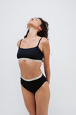 Square Neck Bralette and High Waist Brief in black worn by female model standing with her head stretched back and arms behind her back.  