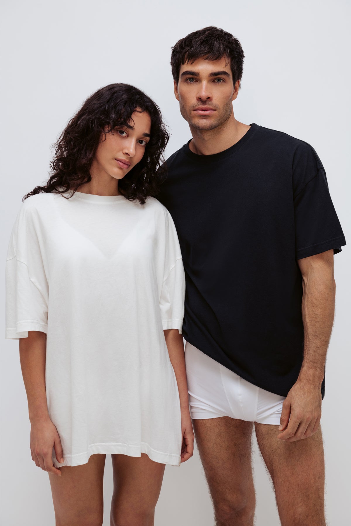 White Oversized Tee with a drop-shoulder silhouette made in organic cotton jersey worn by female model and Black Oversized Tee and White Original Boxer Briefs worn by male model, front view