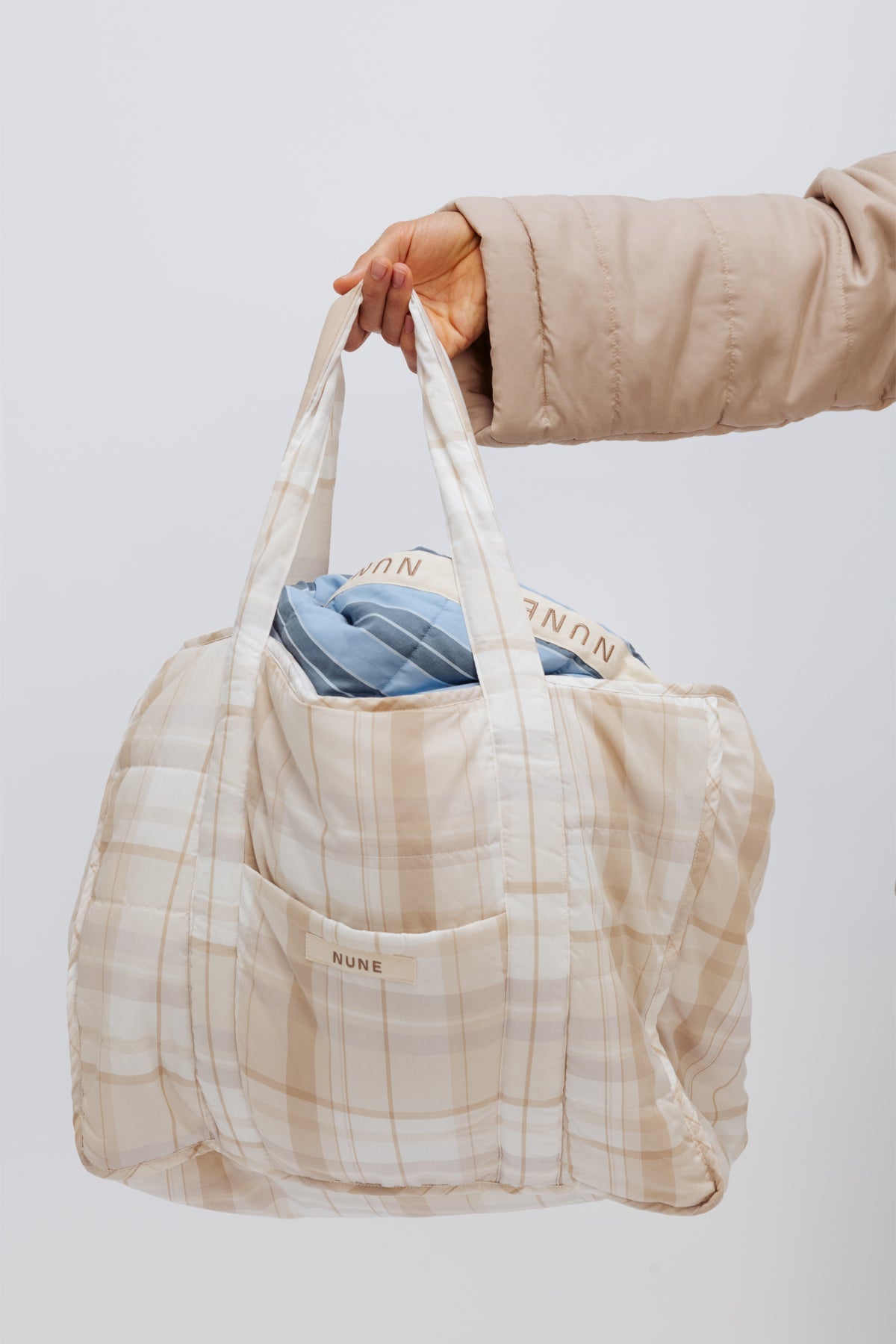 Oat Check Doona Tote being held by female hand, with Daybreak Stripe Short Doona Robe visible inside bag