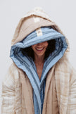 Long Doona Robes in Daybreak Stripe and Oat worn layered by female model smiling, close up view showing hood with NUNE labels