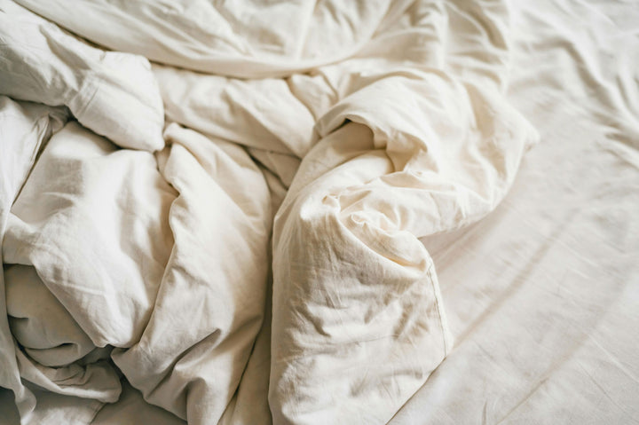 Close up of crumbled natural white sheets and doona on bed
