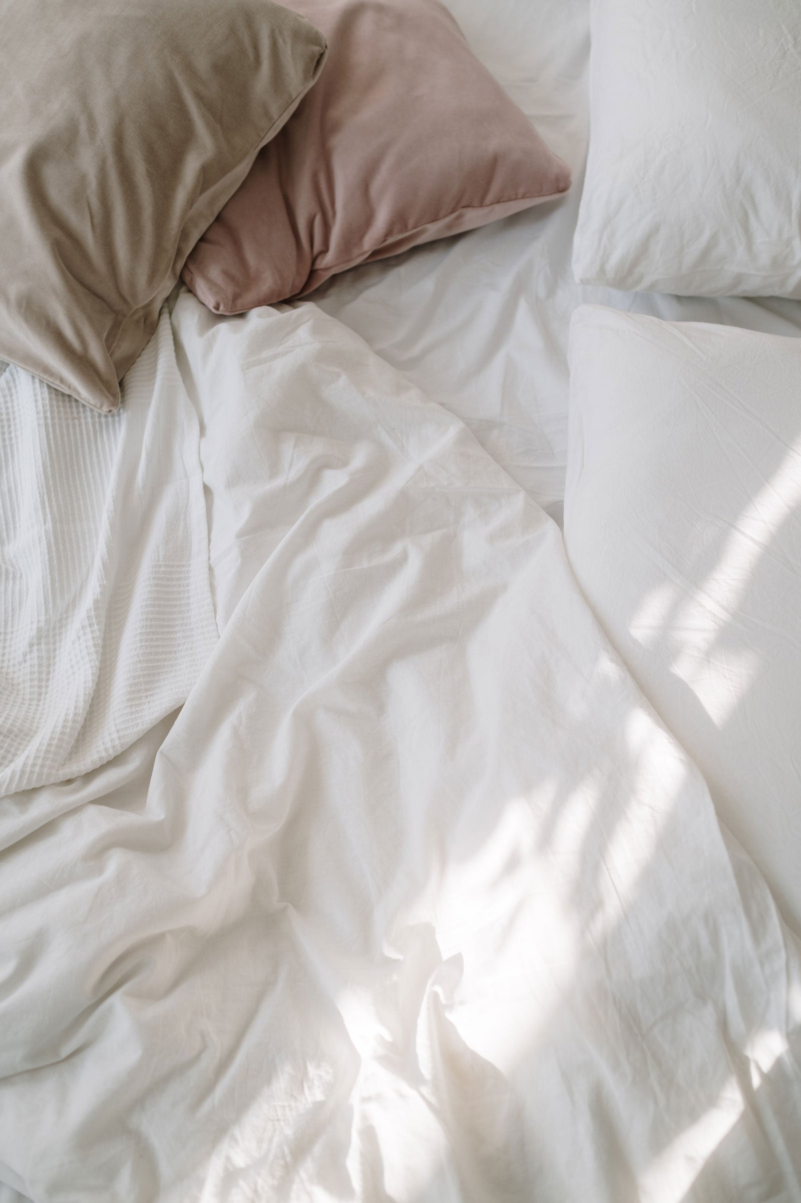 Close up of bed with white sheets, pillows and blush and latte cushions